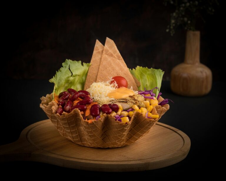 A mouth-watering waffle bowl salad filled with fresh vegetables and toppings on a wooden board.